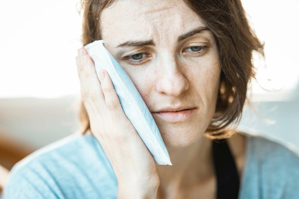 Woman with toothache holding cold compress to cheek.