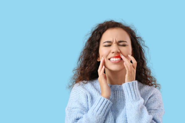 Woman with curly hair touching face near mouth in pain.