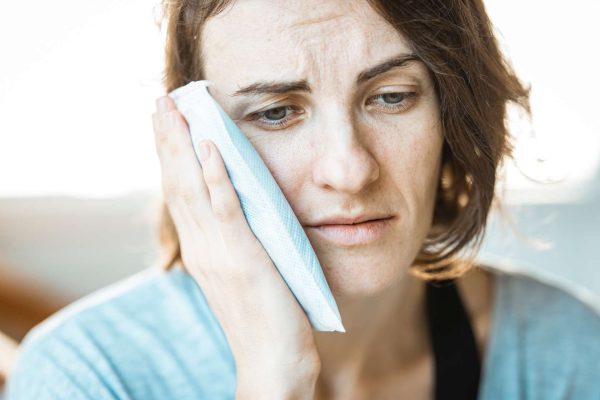 Woman with toothache holding cold compress to cheek.