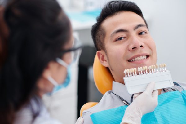 Dentist using special palette when choosing teeth color of smiling male patient before making veneers