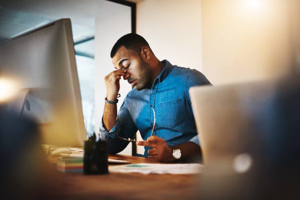 Man pinching bridge of nose in stress while sitting in front of work computer.